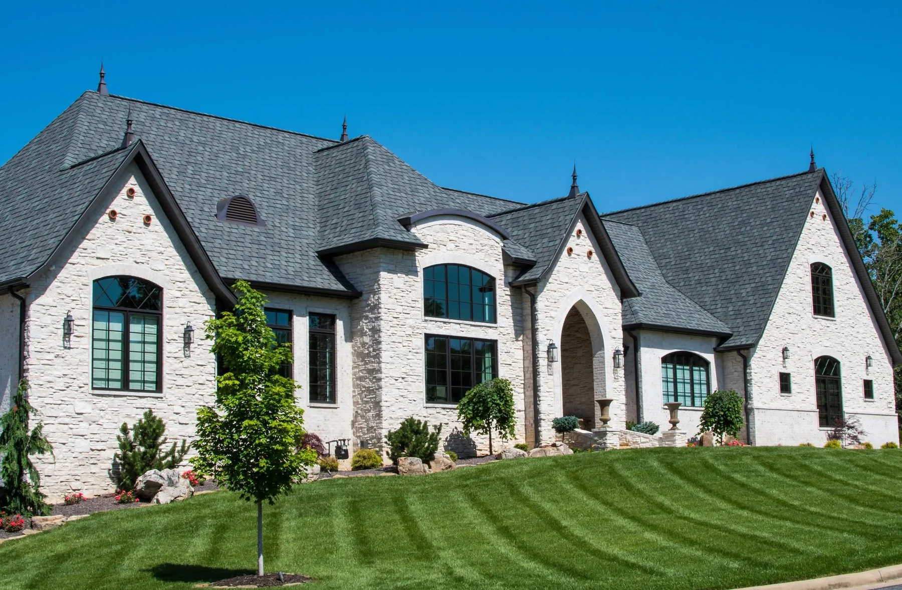 Finished white stone custom home with landscaping and lawn
